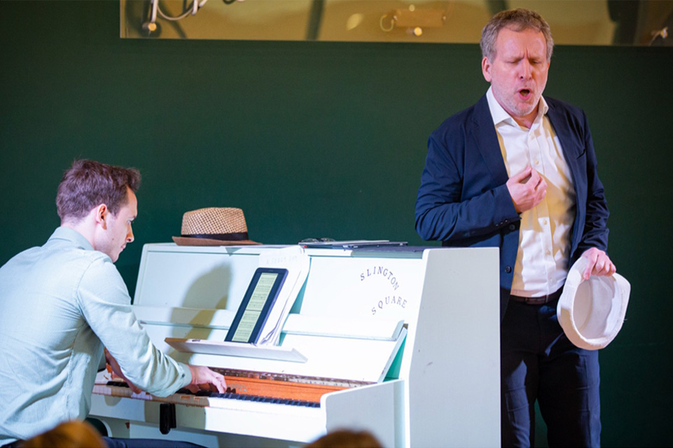 a singer and a pianist performing; pianist wearing a blue shirt, looking at the sheet music on an iPad; singer is wearing a blue blazer, a white shirt and a blue trouser